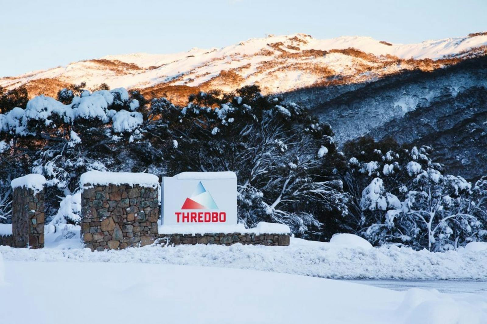 白雪皑皑的山景前有“Thredbo”的标志，背景是白雪皑皑的树木和山丘。