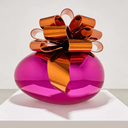 En glänsande magentaskulptur som liknar en insvept gåva med en orange metallbåge, som visas på en vit piedestal.