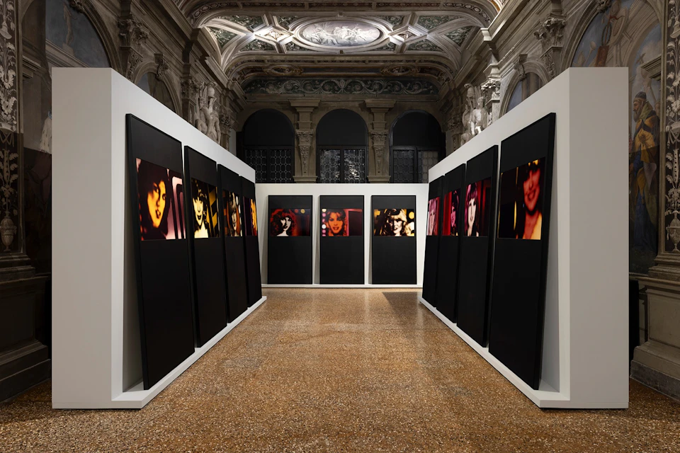 Art exhibition in an ornate gallery, featuring dark panels with colorful portraits displayed along the walls.