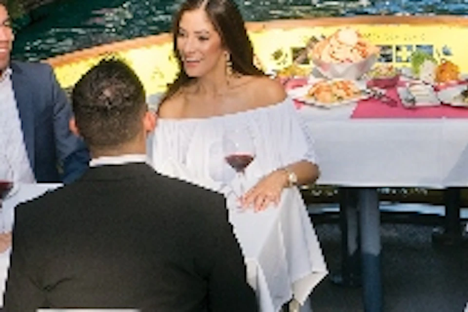 People dining on a boat beneath a stone bridge on a canal, surrounded by greenery in a sunny outdoor setting.
