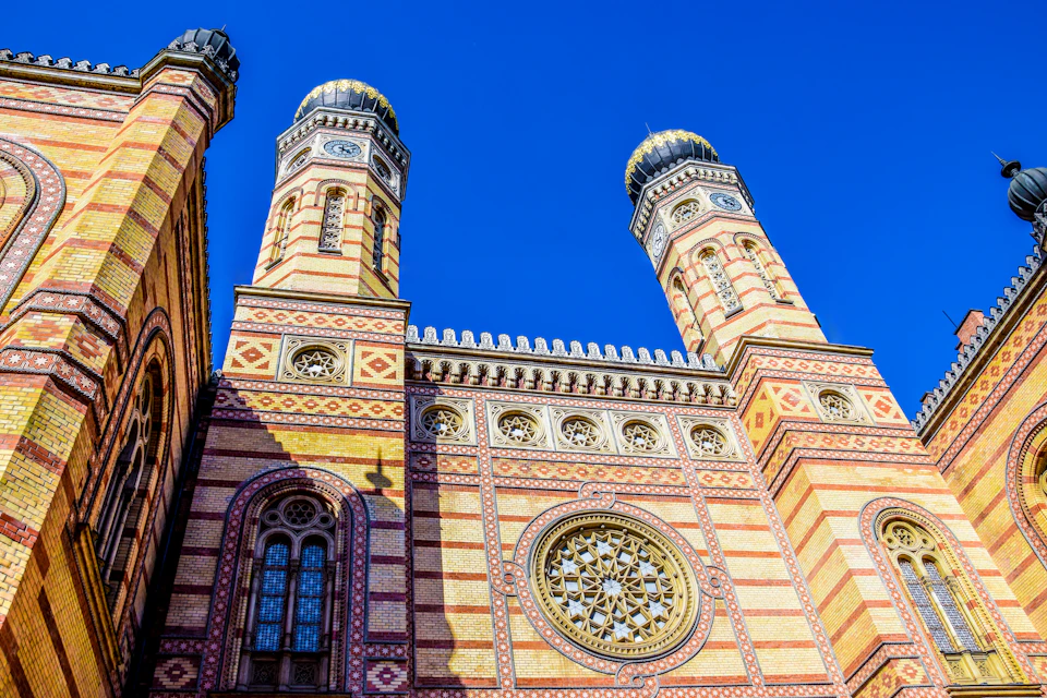Ornate building facade with striped brickwork, twin domes, intricate windows, and a large rose window against a clear blue sky.