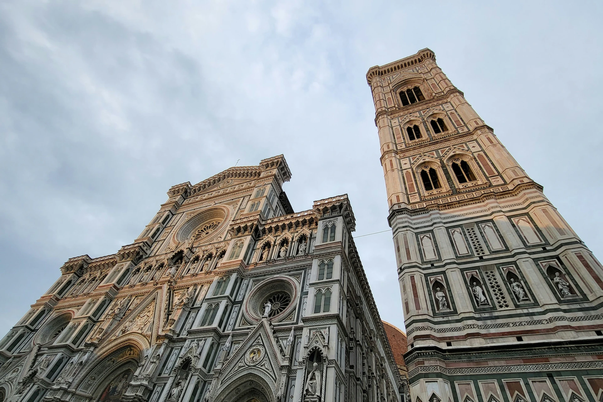 A close-up view of an ornate cathedral facade and a bell tower under a cloudy sky.