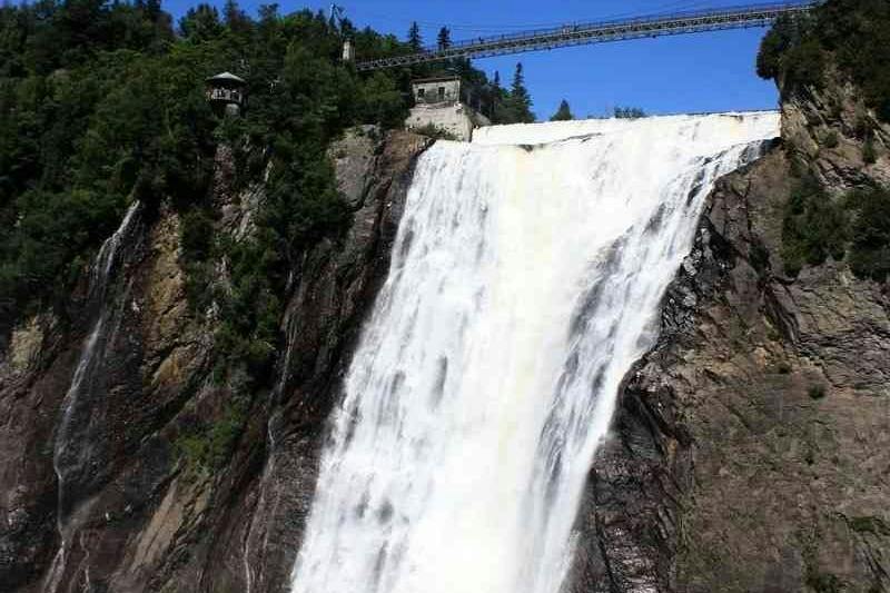 A large waterfall cascading down a rocky cliff with a bridge spanning across the top and trees surrounding the scene.