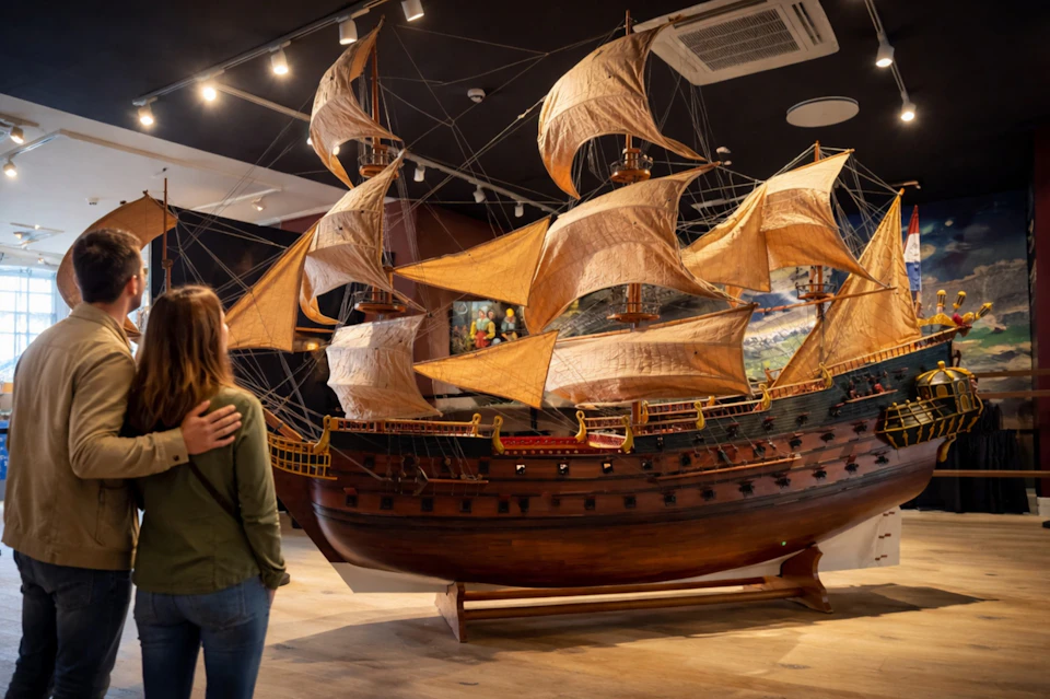 A detailed model of a historical sailing ship displayed in a museum with a person viewing it from the left side.