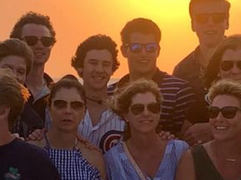 A group of people posing on a boat deck at sunset, with the ocean in the background and a person taking a photo.