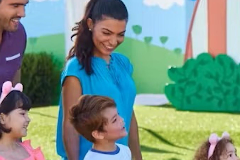 A family with two adults and three children standing on grass in an outdoor play area, interacting with a costumed character.