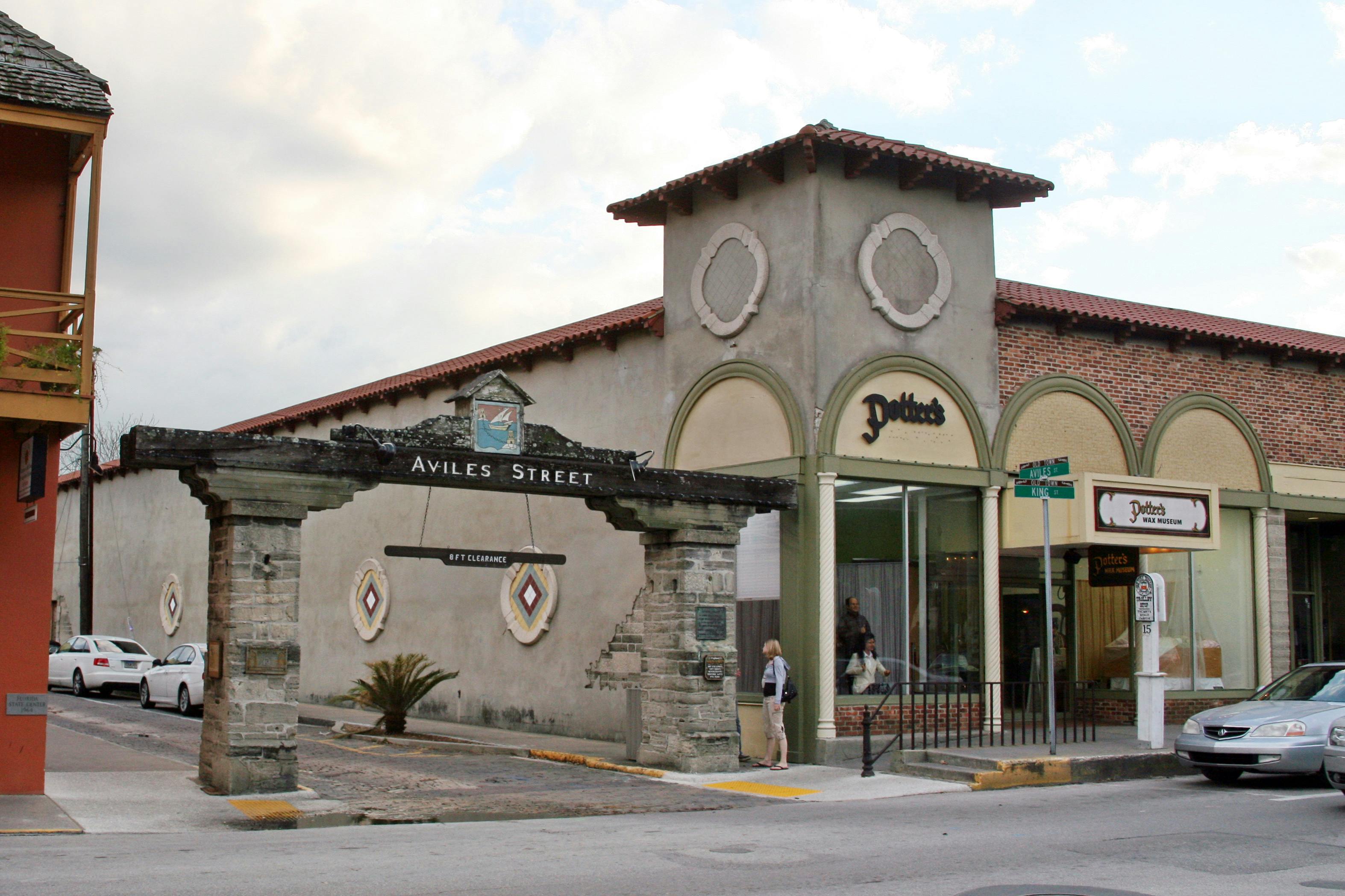 Aviles Street sign with stone archway, adjacent building labeled "Potter's Wax Museum," people and cars are visible on the street.