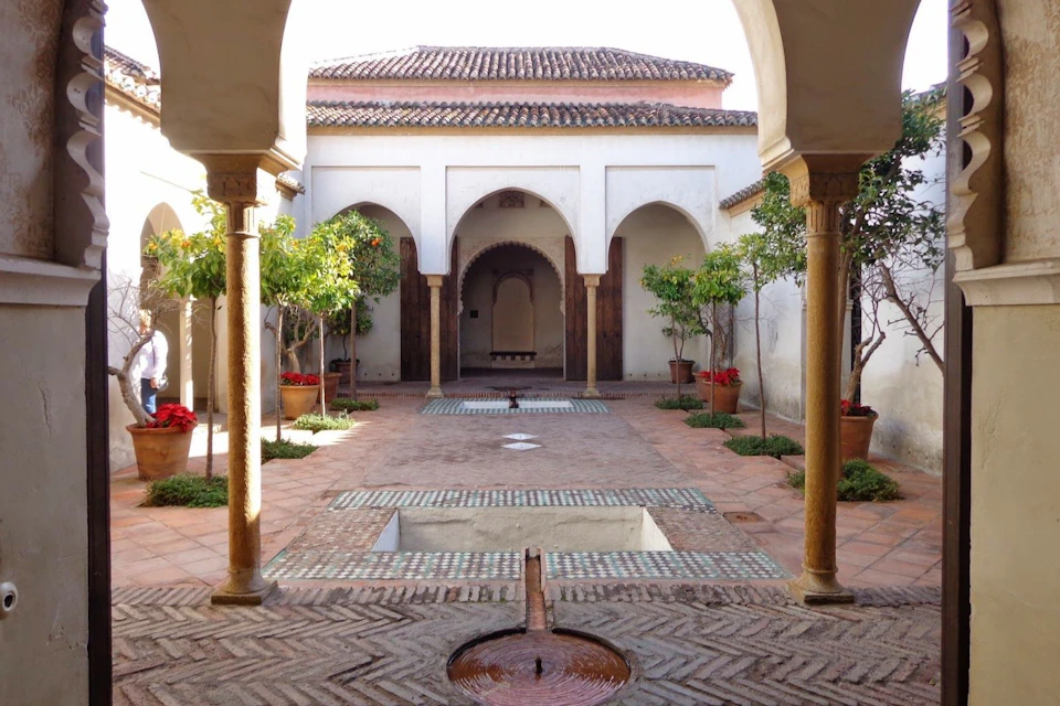 Courtyard with arched doorways, trees in pots, and central water features surrounded by patterned tiles.