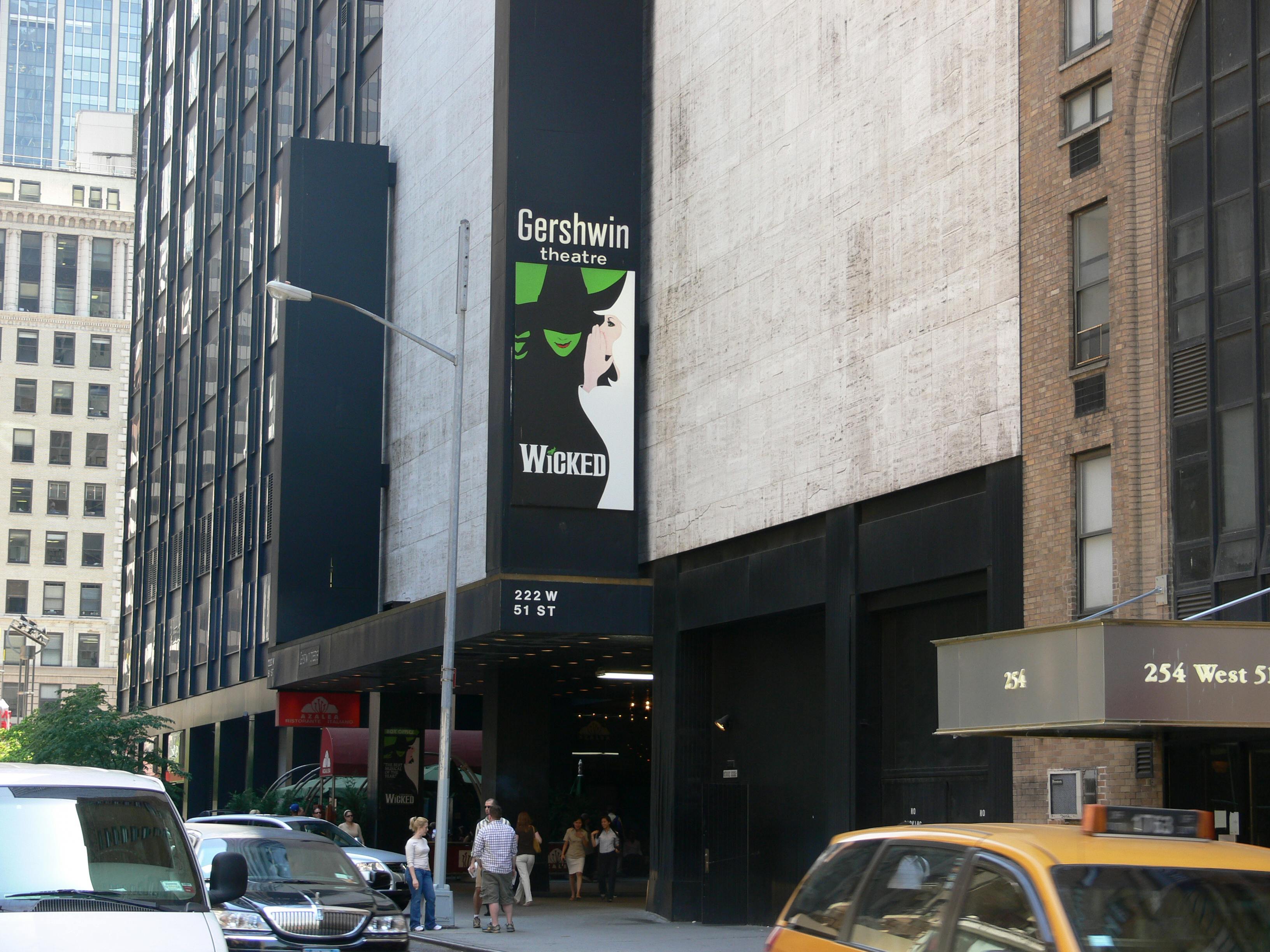 Street view with the Gershwin Theatre entrance on West 51st Street, featuring a poster for the musical "Wicked." Yellow cab and pedestrians present.