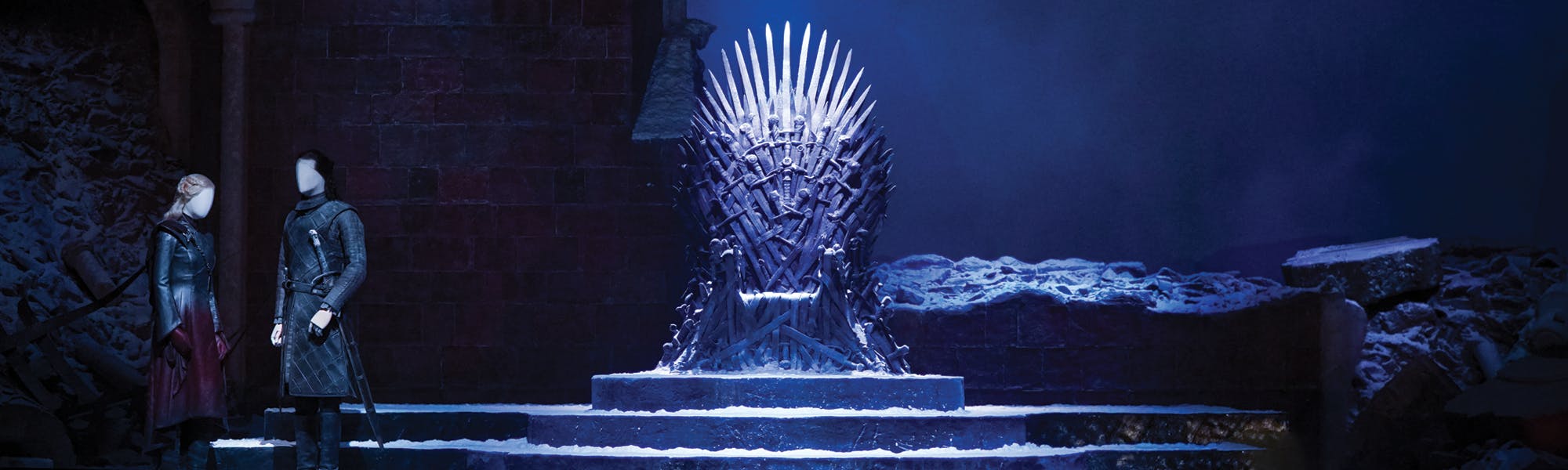 两名身着中世纪风格服装的无脸模特站在昏暗的白雪皑皑的宝座旁。