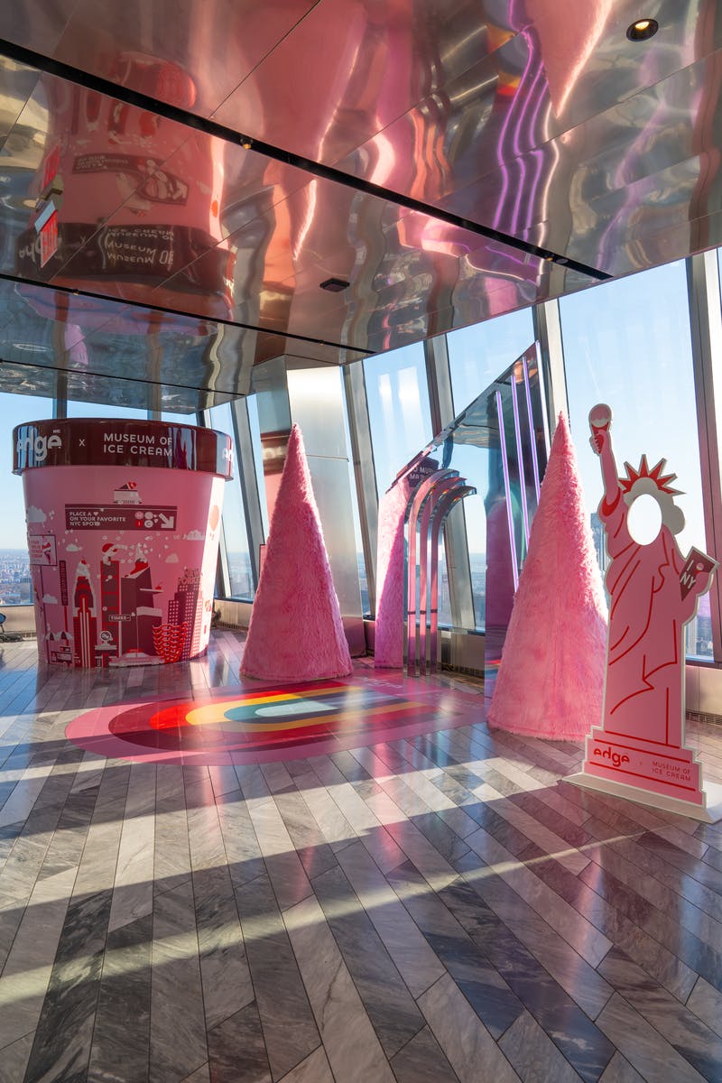 Barevná expozice v budově s růžovými stromy, designem duhové podlahy a výřezem Sochy svobody.