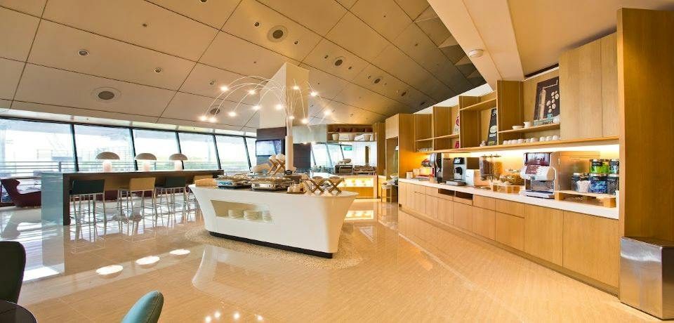 A modern buffet area with a central island, shelves, coffee machines, and large windows providing natural light.