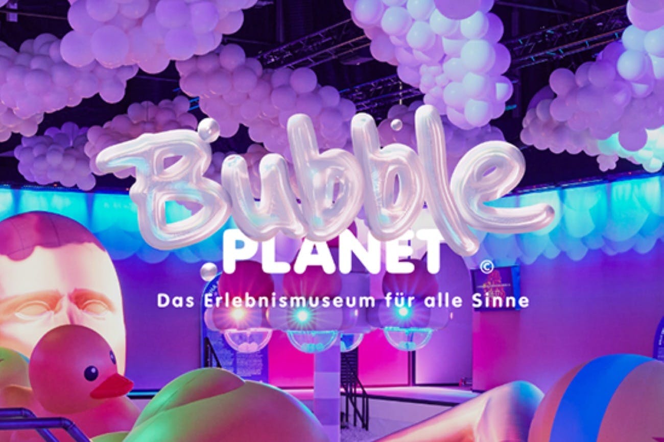 Wyświetlacz z tekstem „Bubble Planet” i „Das Erlebnismuseum für alle Sinne”, z kolorowymi światłami i białymi balonami.