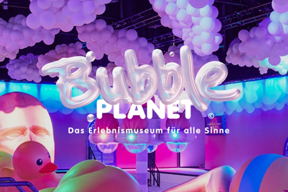A display with the text 'Bubble Planet' and 'Das Erlebnismuseum für alle Sinne,' featuring colorful lights and white balloons.