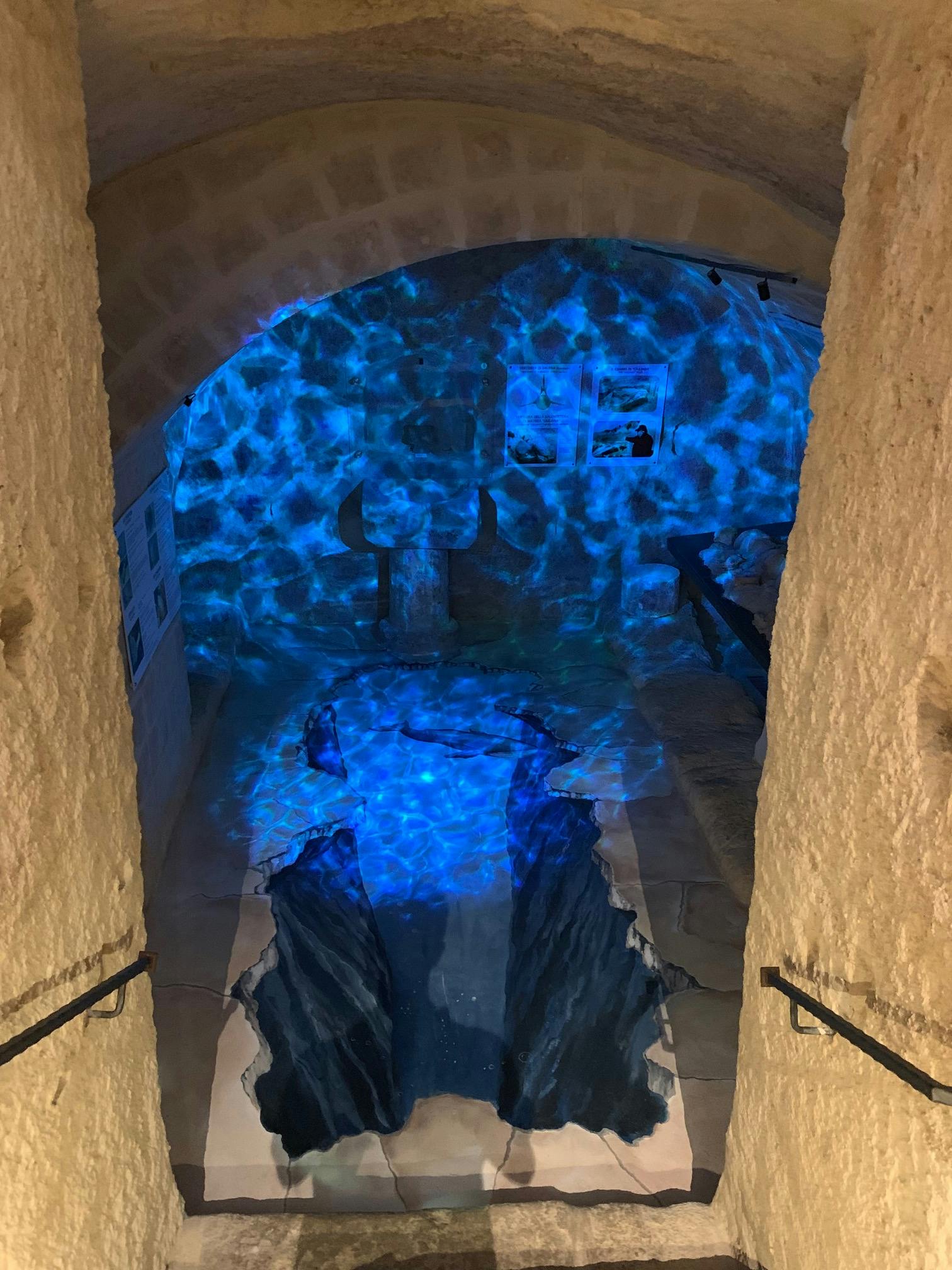 Una stanza simile a una caverna con pareti in pietra, una sottile illuminazione blu e un gioco d'acqua che ricorda un piccolo fiume interno.