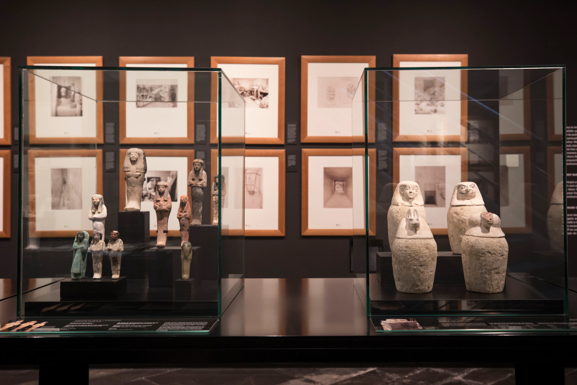 Various ancient artifacts in glass cases on display in a museum, with framed sketches on the wall in the background.
