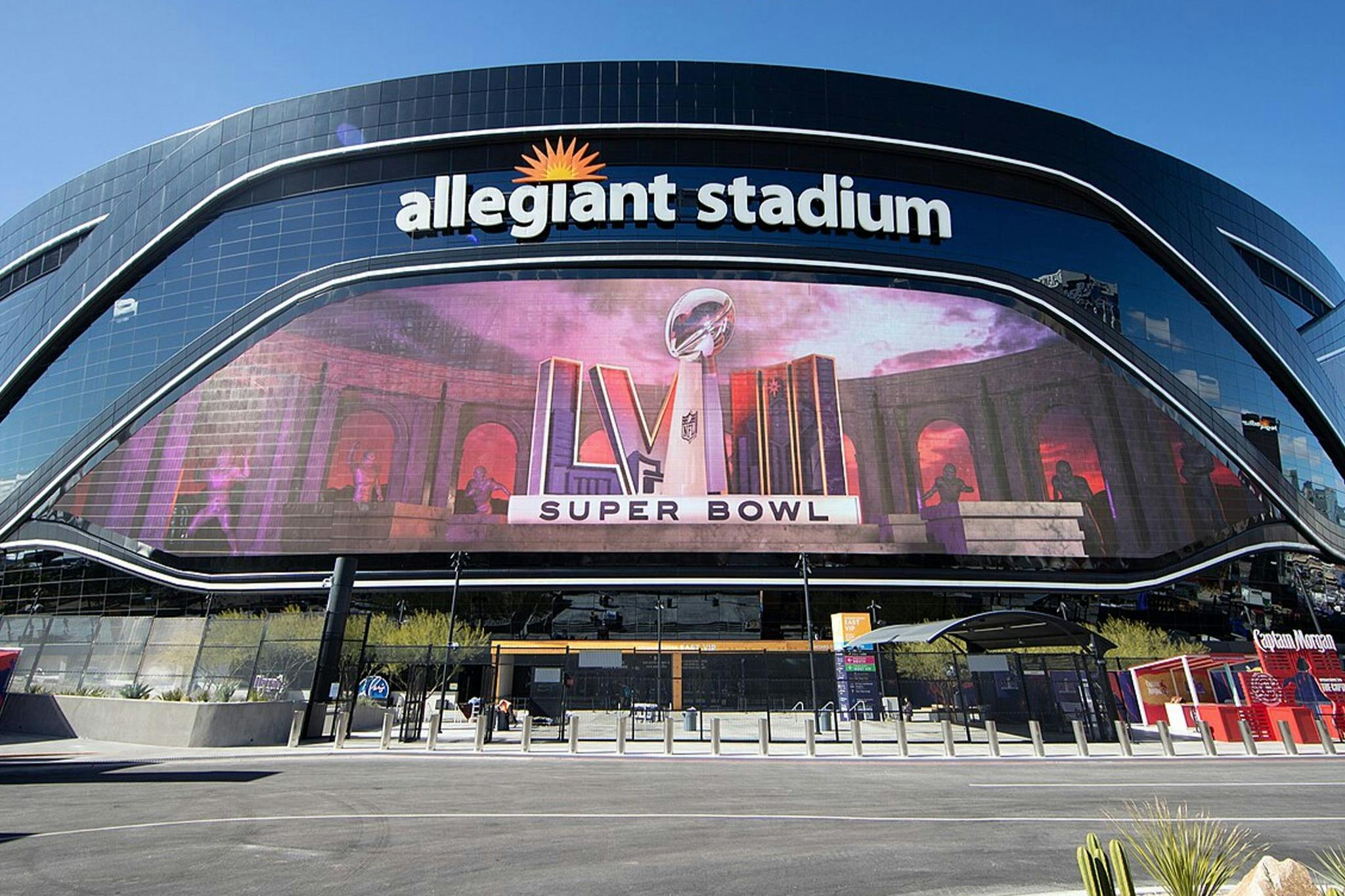 The Allegiant Stadium facade with a large display promoting Super Bowl LVIII, with a clear blue sky visible above.