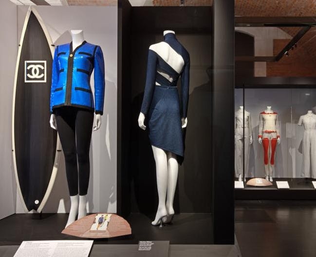박물관 진열대에서 하이패션 의상을 선보이는 마네킹. 블랙 팬츠와 컷아웃 다크 드레스가 돋보이는 블루 재킷입니다.