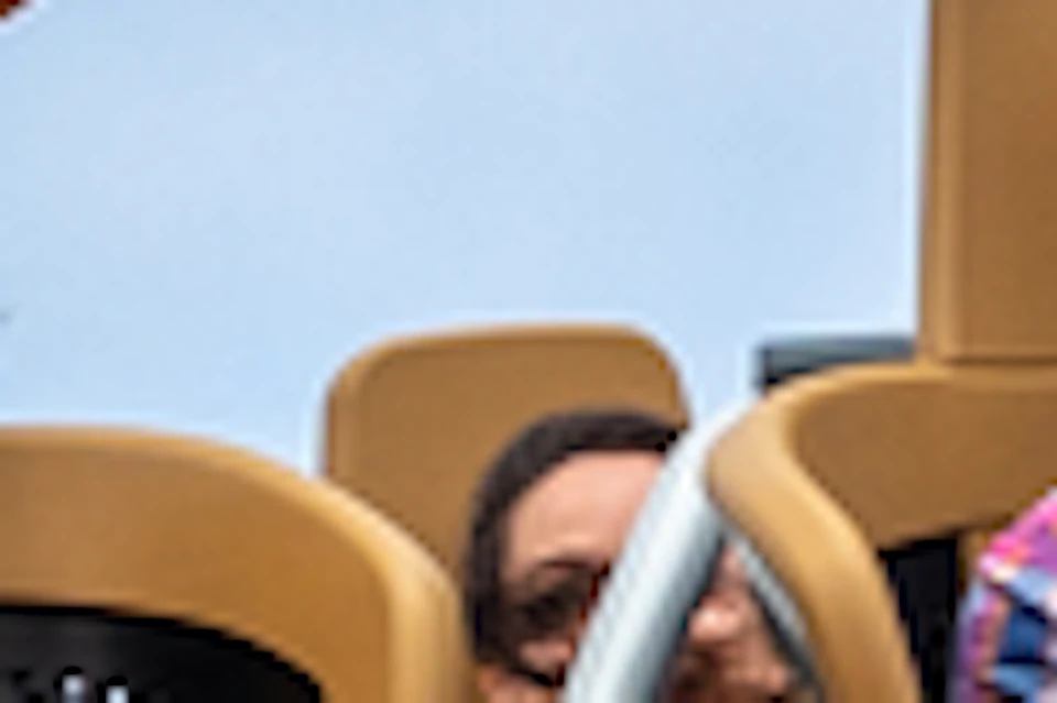 A group of people riding an inverted roller coaster themed as an airplane next to a tall tower under a blue sky.
