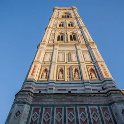 Ett detaljerat, utsmyckat klocktorn med statyer och invecklade mönster mot en klarblå himmel, sedd från en låg vinkel.