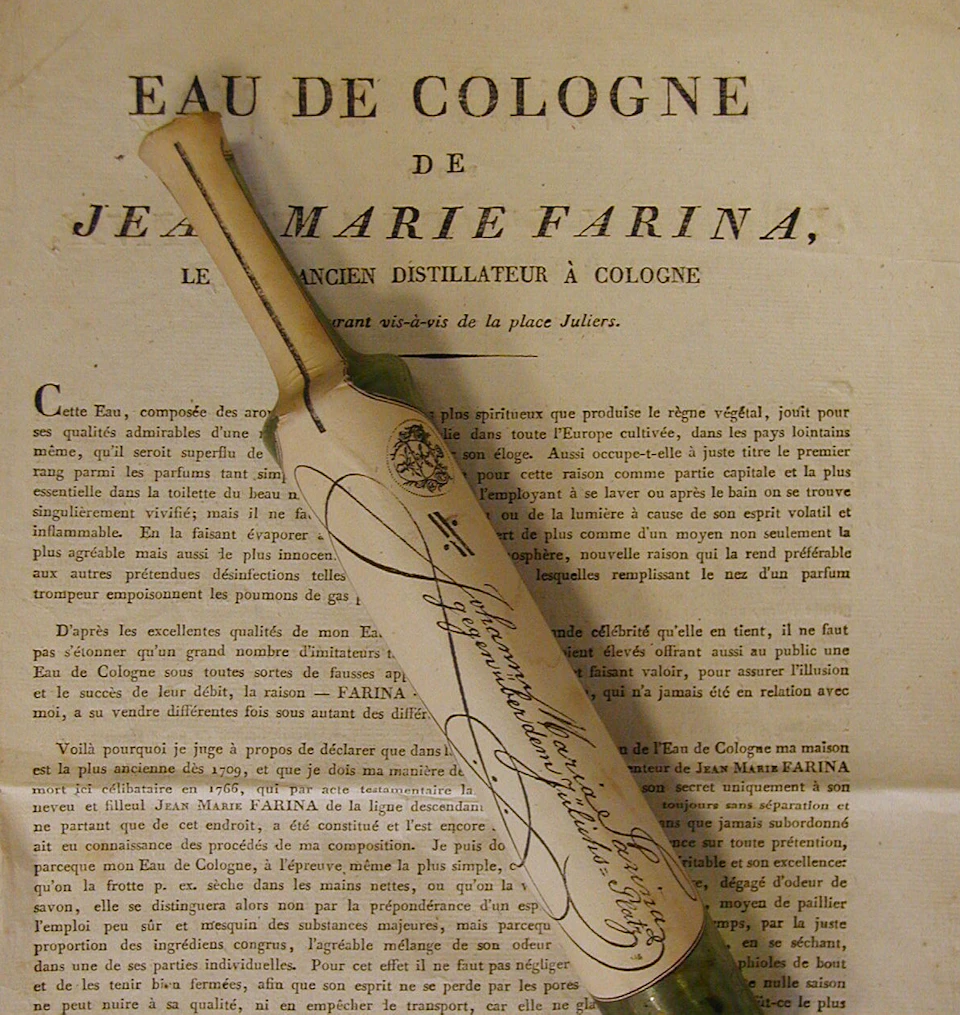 A vintage bottle of eau de cologne wrapped in paper, alongside a printed document with French text detailing "Jean Marie Farina."