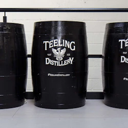 Tre svarta fat med "Teeling Distillery" -logotyper, arrangerade i rad mot en vit tegelvägg.