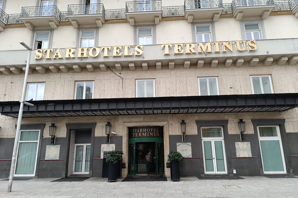 Facade of Starhotels Terminus with a central entrance flanked by large windows and potted plants, set under a beige building with balconies.