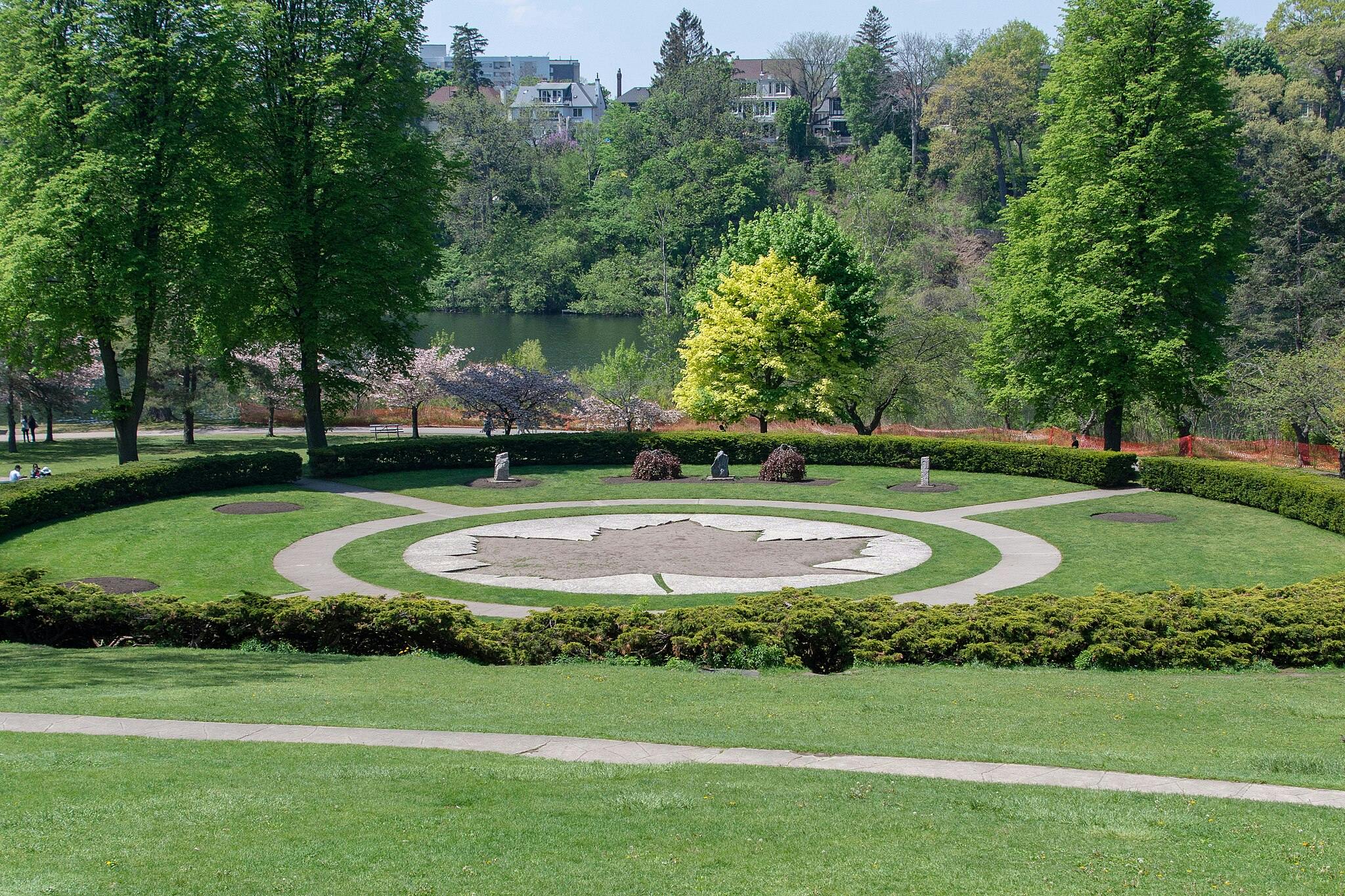 Circular garden with a leaf-shaped design in the center, surrounded by green lawns, trees, and a walking path.