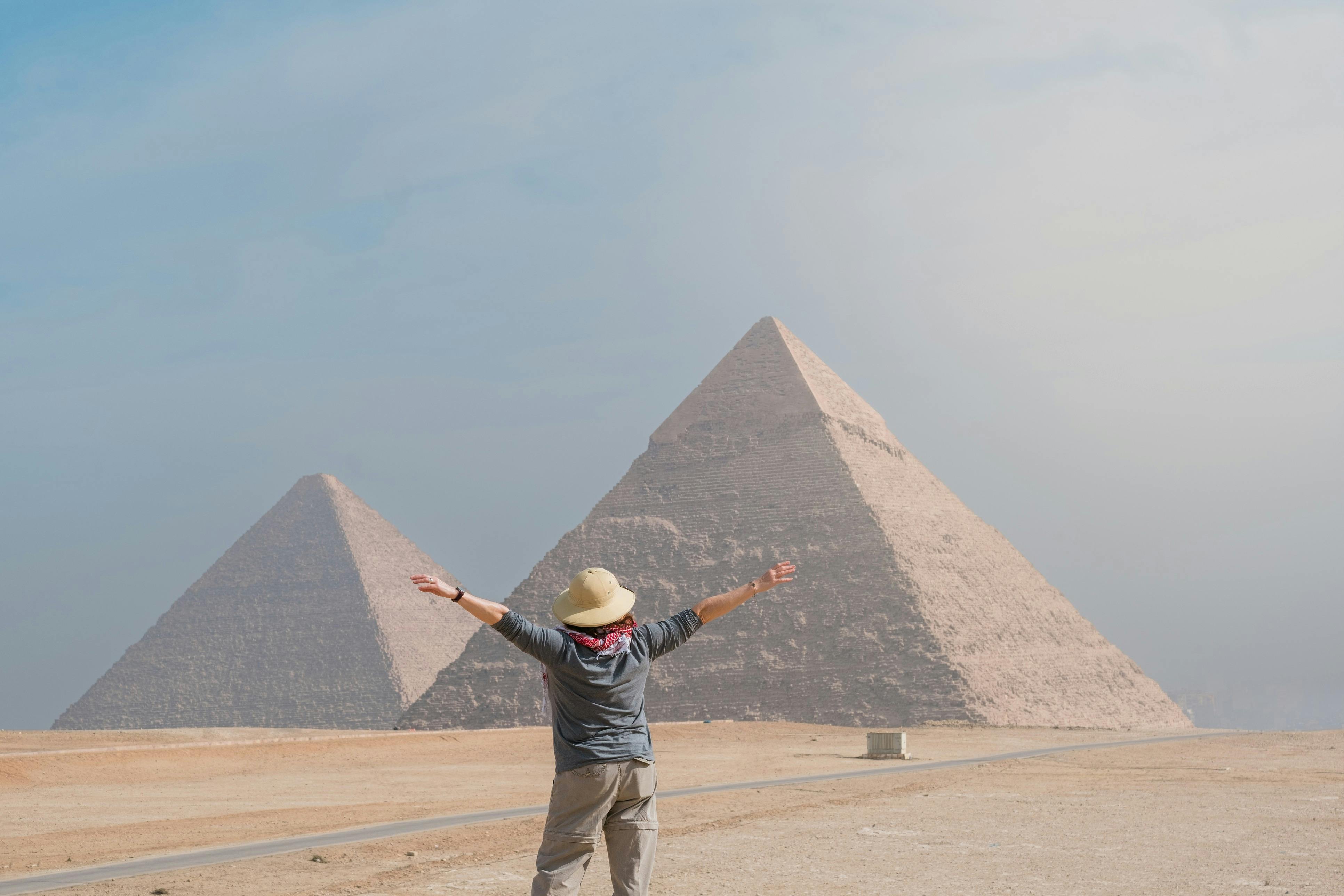 Person with outstretched arms facing the pyramids of Giza on a clear day.