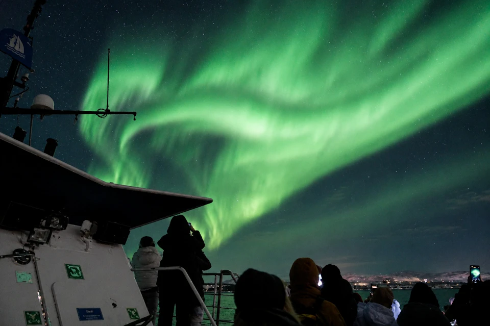 People on a boat viewing the vibrant green aurora borealis in the night sky.