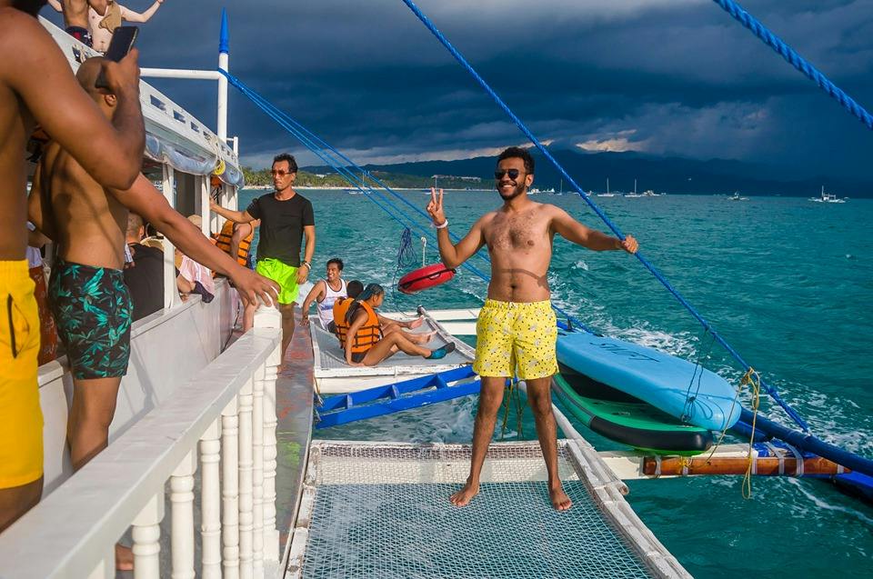 People enjoying a boat trip on the sea. A man poses on a netted platform while others relax on the boat.