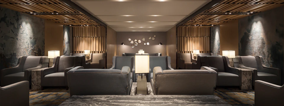 A modern lounge area with gray armchairs, a central table, and decorative wall elements under soft ceiling lighting.