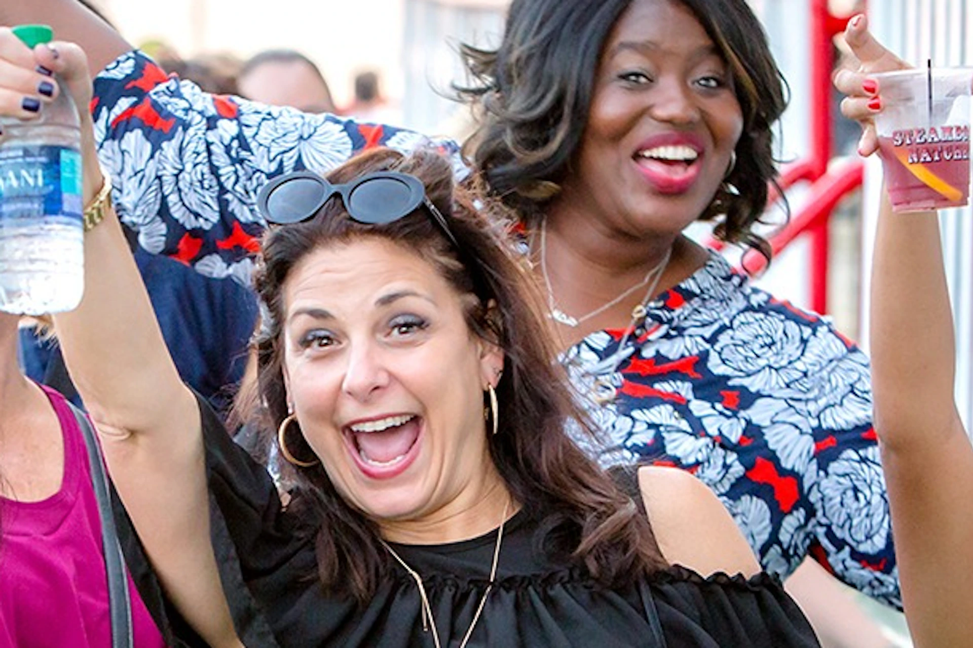 A group of people smiling and raising drinks in a celebratory manner in an outdoor setting with railings in the background.