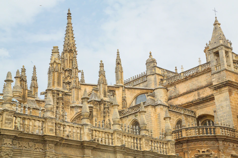Gothic architectural details of a historic cathedral with tall spires, pointed arches, and intricate stonework under a cloudy sky.