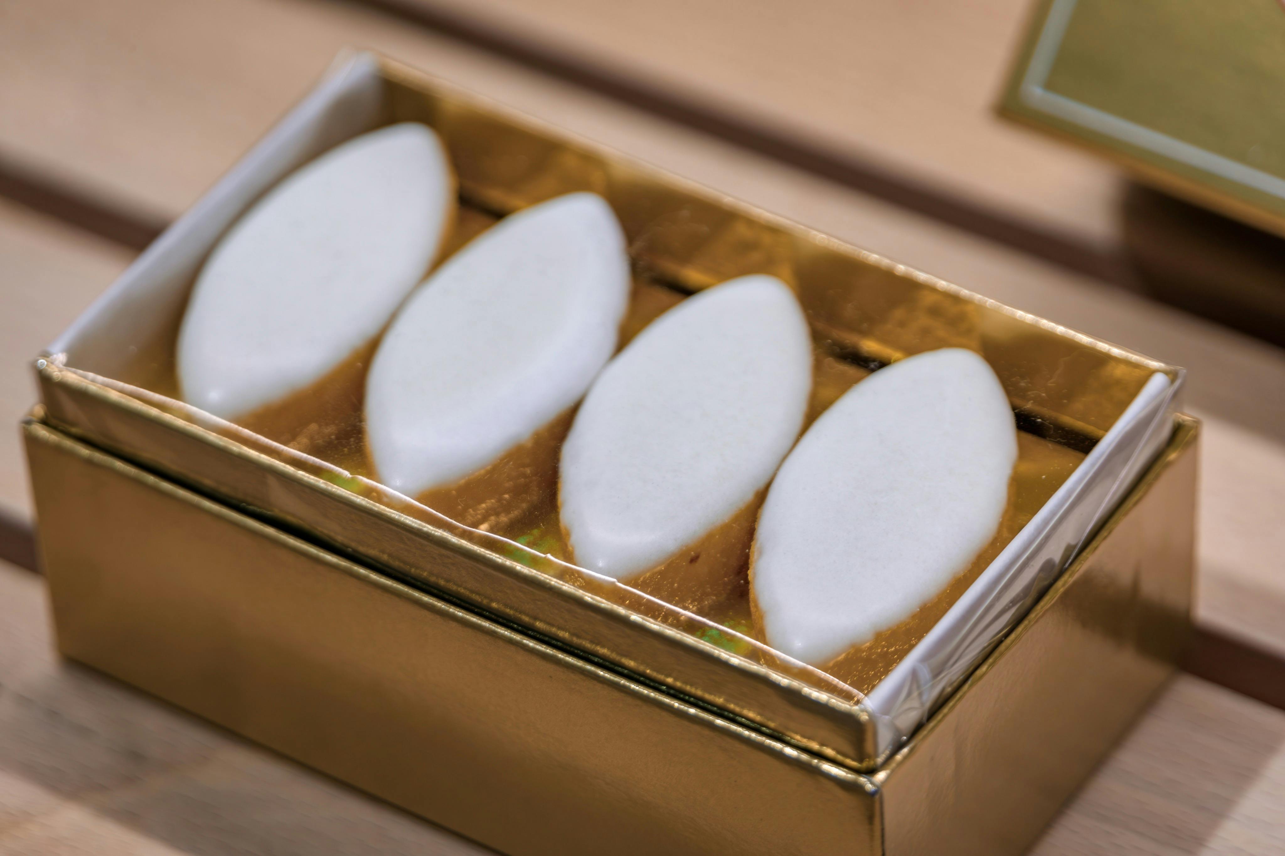 Quatre bonbons blancs de forme ovale disposés dans une boîte dorée.