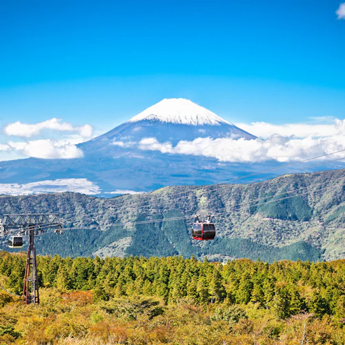Cable cars suspended over a forest with Mount Fuji in the background under a clear blue sky.