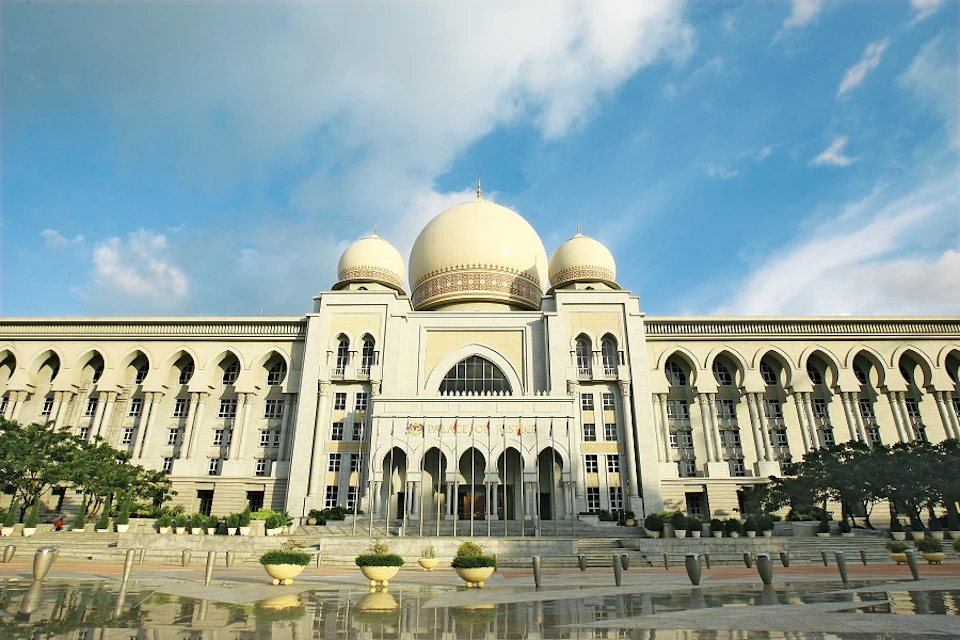 Grand building with large central dome flanked by two smaller domes, arched windows and entrance, under a blue sky.