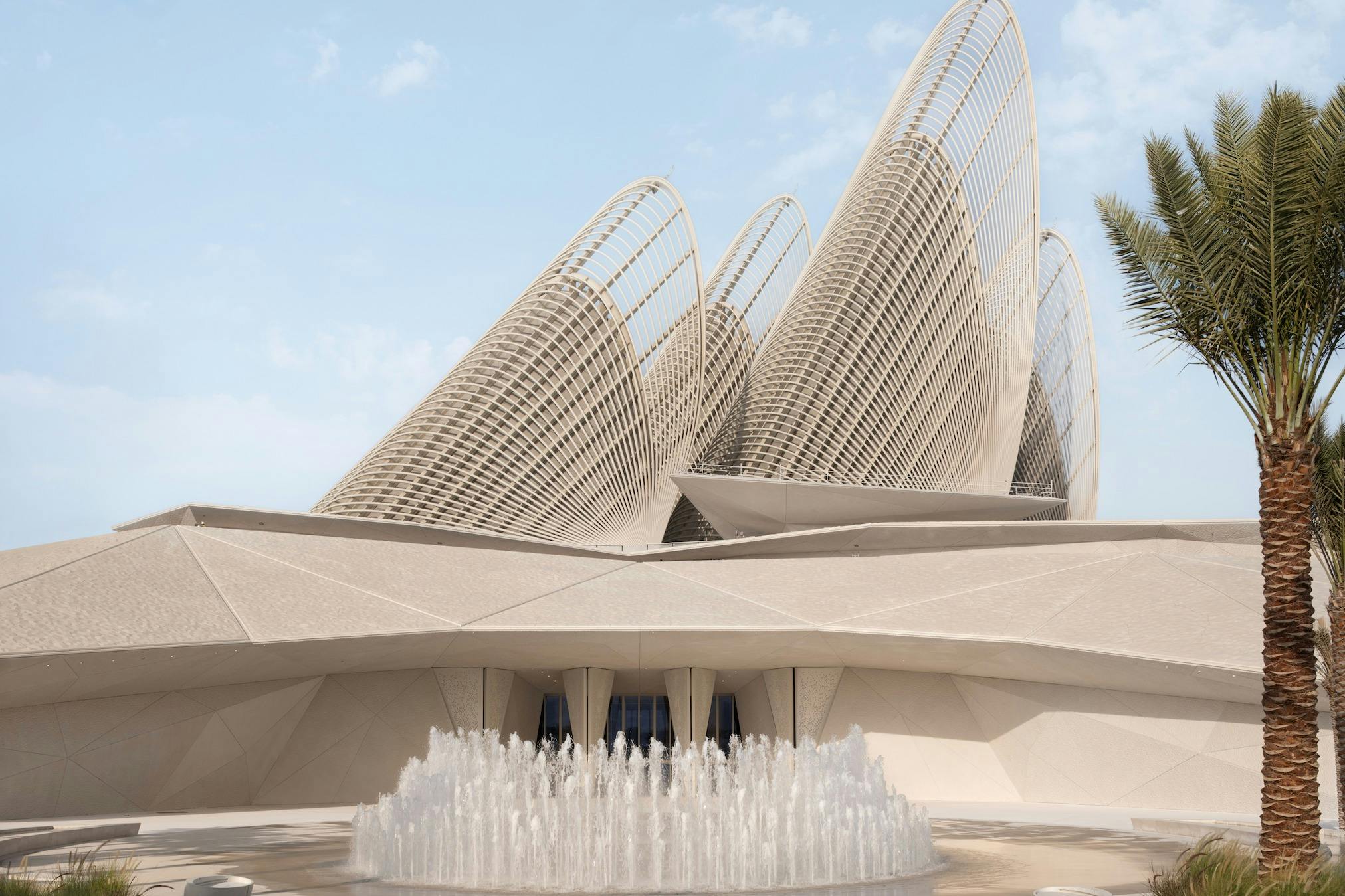 구부러진 격자 모양의 구조물과 맑은 하늘 아래 전경에 분수가 있는 현대적인 건축 건물.