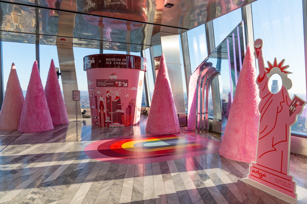 Barevná místnost s růžovými dekoracemi ve tvaru kužele, velkou strukturou s růžovou zmrzlinou a reflexními povrchy.