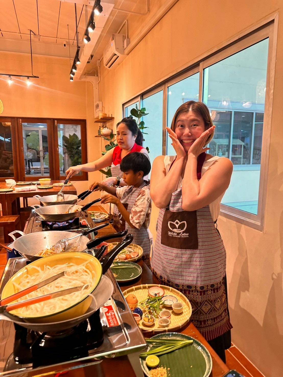 Three people cooking in a kitchen, with a smiling woman in the foreground wearing an apron.
