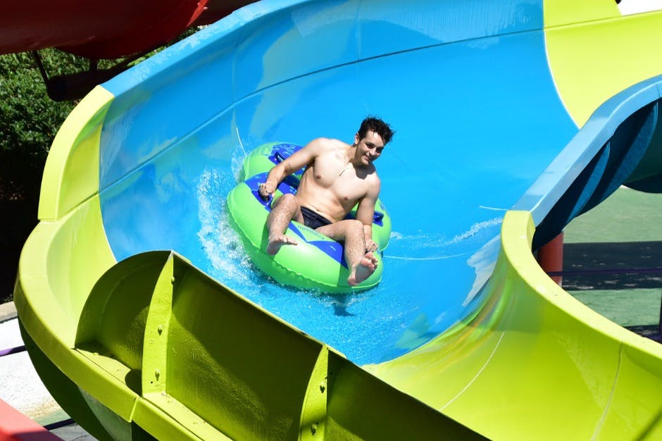 Ένας άντρας καβαλάει έναν πράσινο και μπλε φουσκωτό σωλήνα σε μια πολύχρωμη νεροτσουλήθρα μια ηλιόλουστη μέρα.