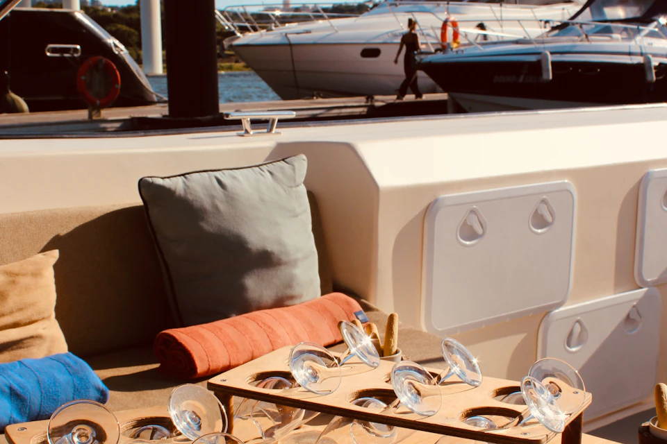 A boat interior with a cushion, a red rolled towel, and a tray holding multiple empty glasses. Other boats are in the background.