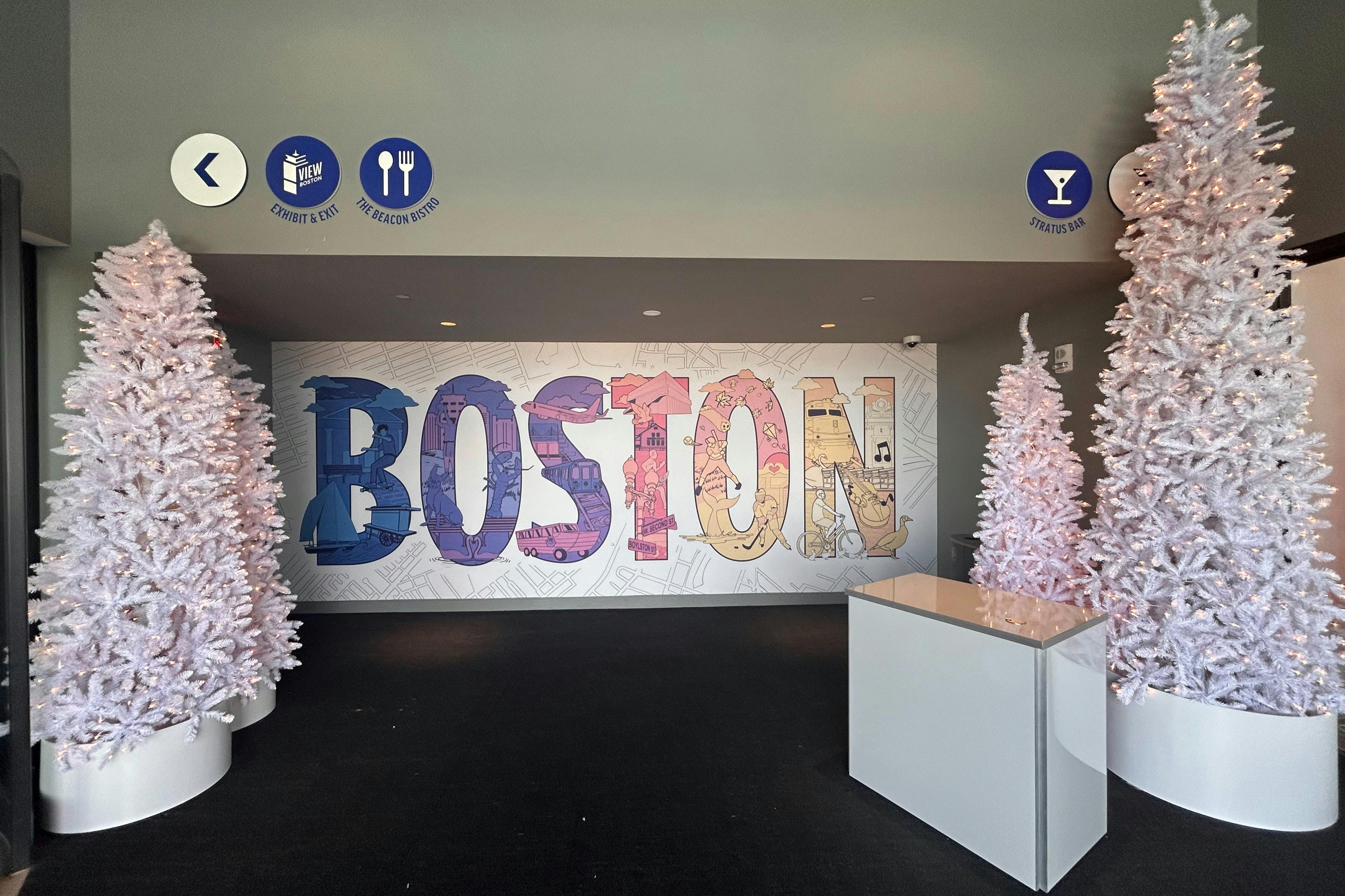 Barevná nástěnná malba „BOSTON“ na zdi, lemovaná dvěma bílými dekorativními stromy a obyčejným bílým pultem v moderním vnitřním prostoru.