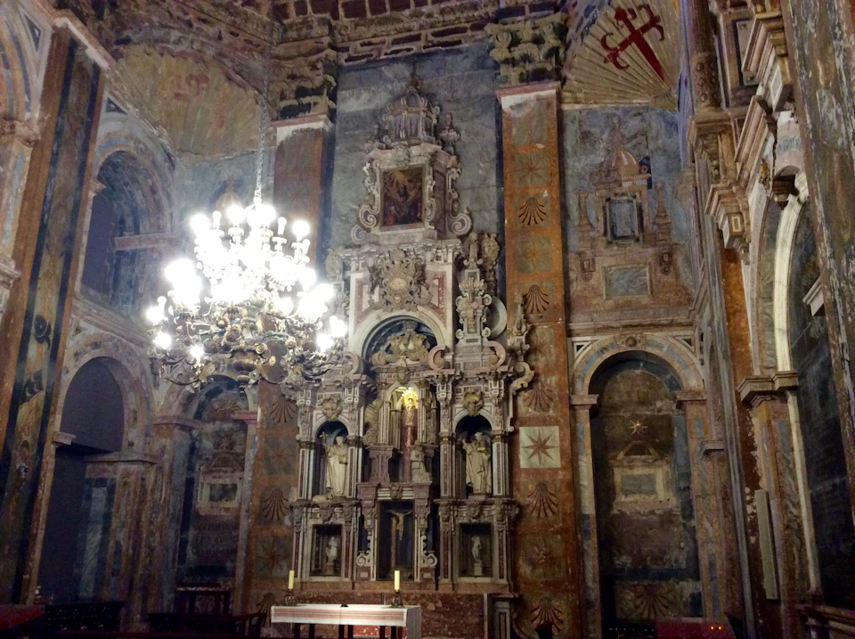 Intricately decorated church altar with statues, murals, and an ornate chandelier hanging from the ceiling.