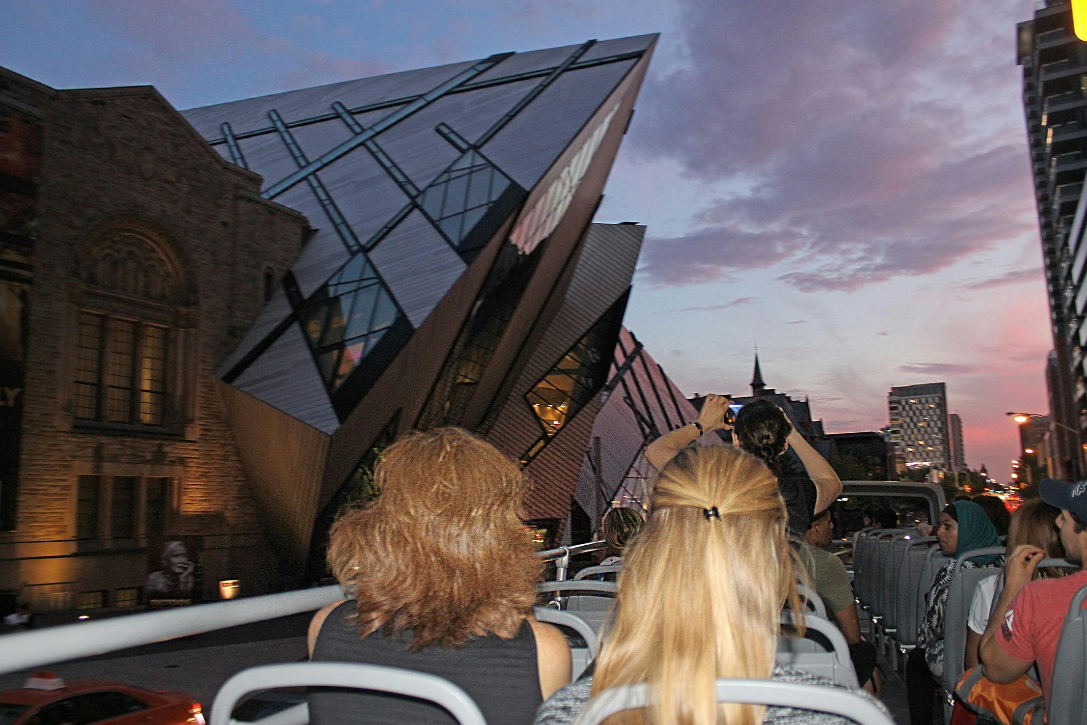 Open top double decker bus approaching the Royal Ontario Museum in the late evening