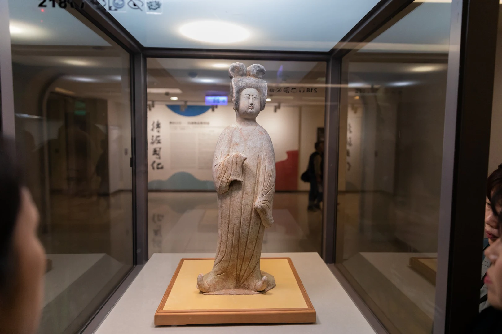 A ceramic statue of a woman in traditional attire, displayed in a glass case at a museum.