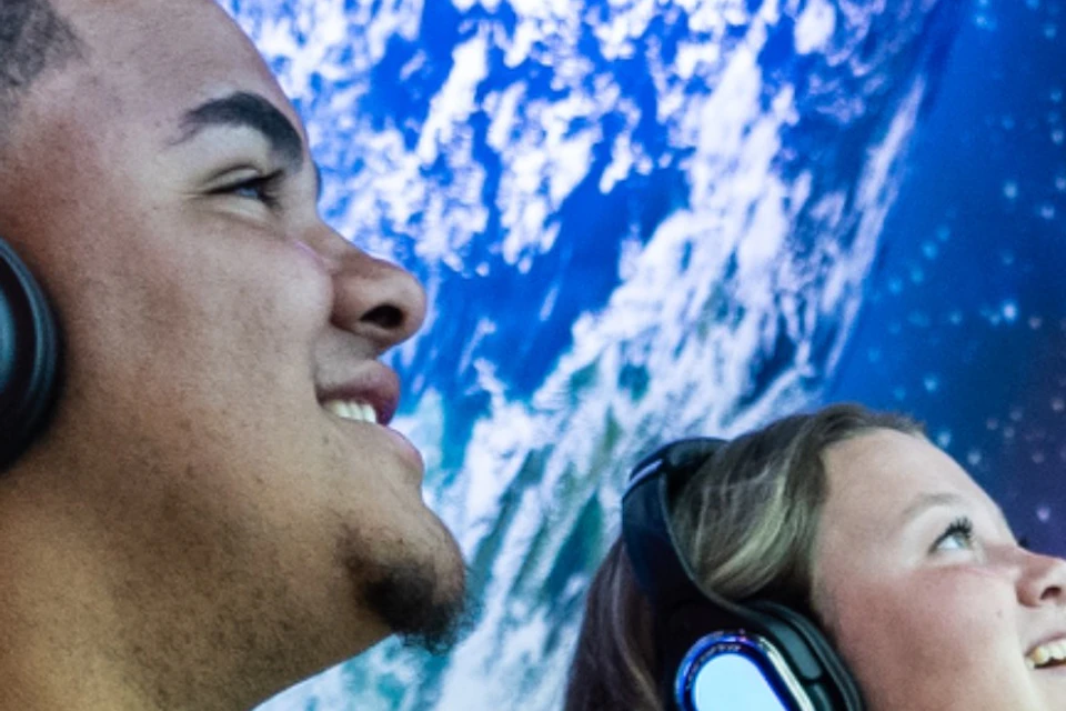 Four people wear headphones and sit in chairs while looking at a projection showing Earth from space.