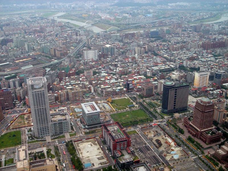 Aerial view of a densely populated urban area with high-rise buildings, roads, bridges, and patches of green spaces.