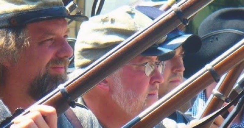 Twee mannen in militaire uniformen en hoeden met geweren in de hand, buiten, in dezelfde richting kijkend.