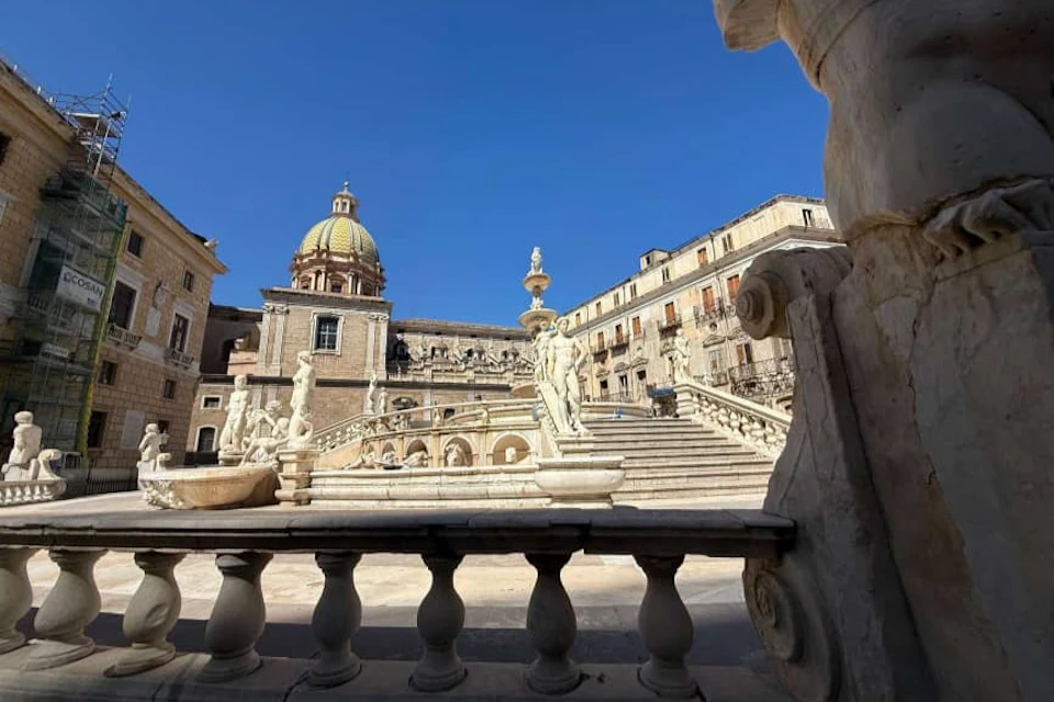 A historic plaza featuring a domed building, ornate staircase, and statues under a clear blue sky.